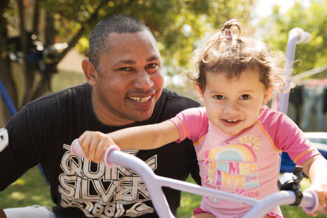 Darren Mercy and daughter Avril Mercy play in the garden outside Galambila Aboriginal Health Service. Photo: Jason Malouin/OxfamAUS