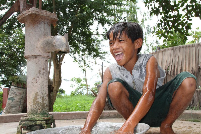 A boy laughs beside a stone water fountain
