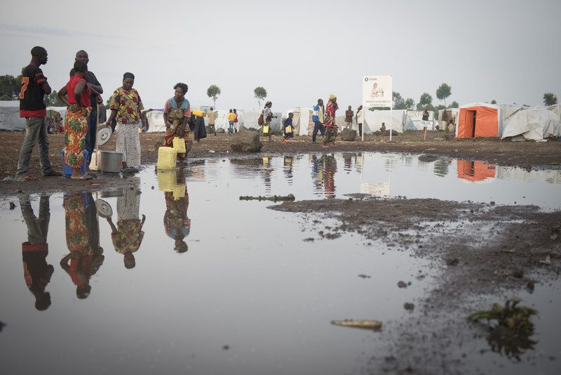 People carrying water containers across a muddy stretch of water