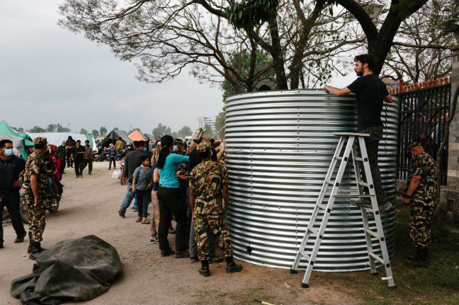 Technical volunteers, trained by Oxfam during the urban risk management program, erect a T11 water tank with a capacity of 11,000 Litres of clean drinking water at the Tundikhel IDP camp in Kathmandu, Nepal. They are assisted by volunteers from Holland, tourists stranded after their flights were cancelled, and members of the Nepali armed forces. Photo: Aubrey Wade. Nepal earthquake Photo: Aubrey Wade