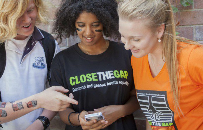 Students huddle around a mobile phone to showcase their interest in the Close the Gap Instagram challenge