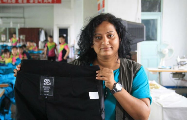 A woman holds up a piece of clothing produced for Rip Curl in the factory where we she works in North Korea