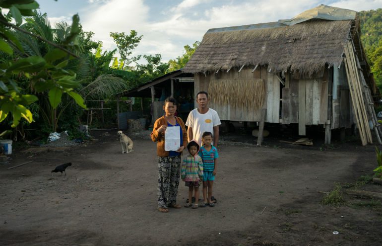 Pis Village, Cambodia: In 2010, Ms Pheun Ra (40) was evicted and forced to move with her family to a resettlement village. She was given a small plot of land (40 by 50 metres) to farm. Holding documents to their land, she stands here with her family in front of their house. Photo: Thomas Christofoletti/Ruom/OxfamAUS. banks and land Thomas Cristofoletti Ruom OxfamAUS_770x495