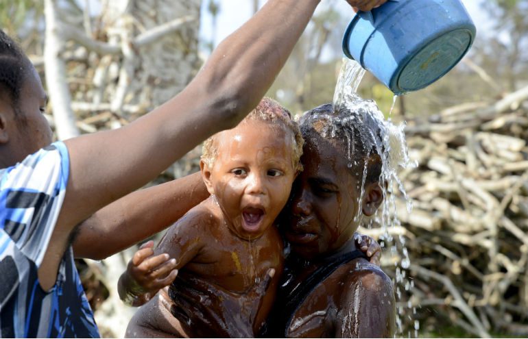 Two kids enjoy a shower as a bucket of water is poured over them in the aftermath of Cyclone Pam, Vanuatu