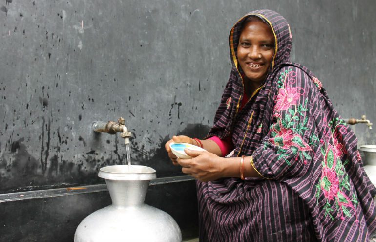 A woman crouches next to a new water tap installed by Oxfam
