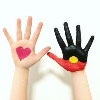 Two hands raised in the air, one Indigenous with the Aboriginal flag painted on, the other a non-Indigenous hand with a love heart painted on.