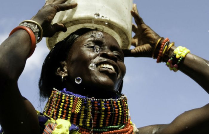 a smiling woman carries a bucket of water on her head