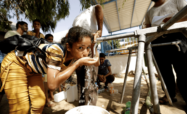 A young girl drinks water from an Oxfam tap stand.