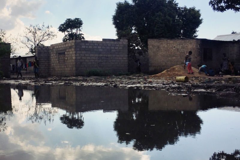 Photo above: In the dry season, this peri-urban settlement has stagnant water everywhere. People hop from stone to stone to avoid it. Others have no choice but to use water like this to wash their clothes and dishes because they can’t afford to miss work and line up for several hours at a tank.