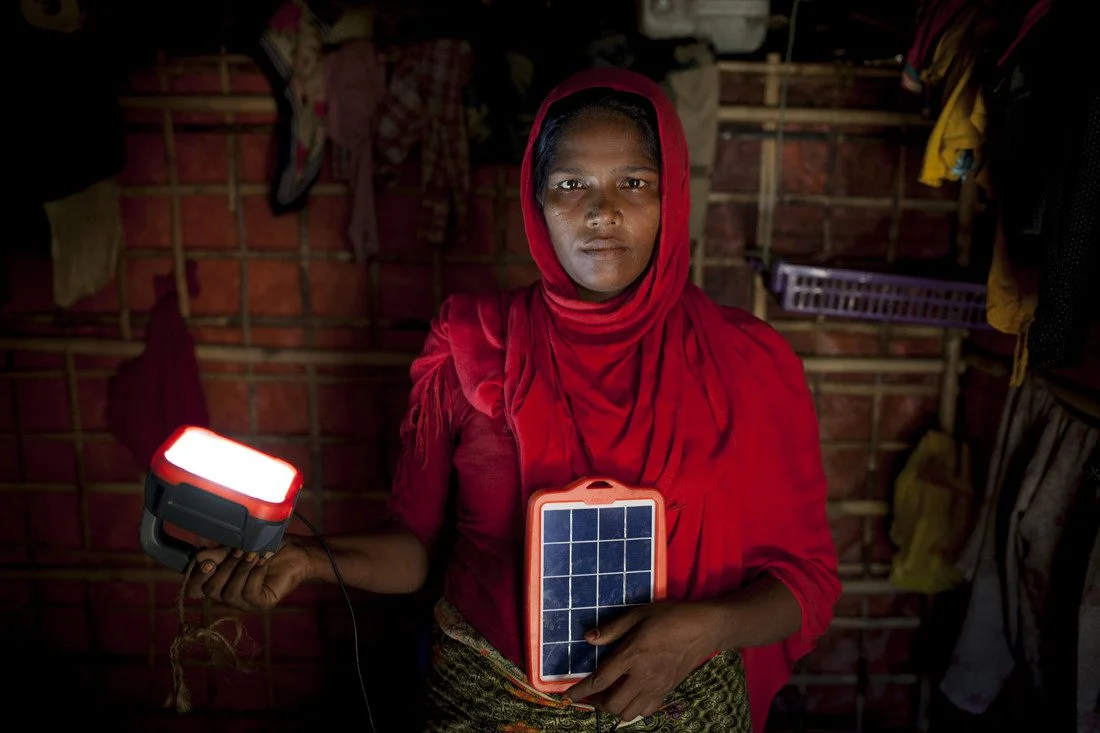 <p>
Rohingya refugee Asia Bibi* with solar powered lamp provided by Oxfam, in her shelter in the camps in Cox’s Bazar, Bangladesh.</p><p>
</p><div>
The family use a latrine and water pump built by Oxfam near to their shelter. Oxfam has also provided Asia and her family with aid including solar powered lamp, food vouchers, and hygiene items such as soap, sanitary cloths, buckets, and toothpaste.</div><div>
</div><div>
Asia: “Life in Myanmar was hard. When my daughter was 40 days old my husband, who worked as a labourer, ran off with another woman. My children both went to a madrasa, a religious school. The Myanmar government stopped Rohingya children going to local schools and about a year before we left they imposed a curfew so we weren't allowed out of our houses in the evening. Because my husband was not around I had to go out and work for other people, such as pounding chillies for cooking. I also used to work for the UN on their local education programmes. </div><div>
</div><div>
We decided to leave Myanmar because our village was attacked. Fire bombs were thrown at our house. We ran and hid in hills for seven days with barely any food or water. After that we walked and hid in a cave for 15 days. When we reached the border we had to pay 10,000 taka (about £90/US$110) per person to cross the river on a boat. The boatman dropped us off on one of the small islands along the border. We eventually reached the camp about seven months ago, in December 2017. </div><div>
</div><div>
When we first arrived in Bangladesh we didn't have any food or money. I had to ask for help from other refugees in order to feed my kids. We suffered a lot at that time. When I think about it now I get stressed and my stomach hurts. </div><div>
</div><div>
Since then we have received help so right now we're in a good situation. I got solar panels from Oxfam so we have electricity for lights at night. Oxfam also gave me some clothes and underwear because I left Myanmar with only the clothes I was wearing, as well as things like toothpaste and soap. Oxfam provided sanitary cloths which can be used for pads which is very helpful because in Myanmar I had to use old rags during my period. I receive monthly food and soap vouchers from Oxfam which I use in designated shops in the camp. I exchange the soap voucher for 18 bars of soap, for washing and laundry. With the food voucher I stock up on things like potatoes, eggs, onions, garlic, chilli. When the kids are running around playing I can make them an omelette or cook them lentils. </div><div>
</div><div>
Oxfam's plastic storage buckets have been a saving grace, especially during the monsoon as I can store rice in one to keep it dry. The toothpaste has made a big difference. The children are very enthusiastic – they clean their teeth four times a day. They have been scrubbing so much I have to tell them to stop otherwise they can't eat the rice because their gums hurt. We also use the latrine and water pump that Oxfam built nearby. </div><div>
</div><div>
Right now we're in a good situation but we did not come here because we wanted aid. We came here because we needed to save our lives.</div><div>
</div><div>
It is hard to be a woman on her own her in the refugee camp. It is a big problem when you don't have a husband or a male figure around. As well as cooking, cleaning, fetching water and looking after the children, I have to do all the jobs men usually did in Myanmar. I have go out to get rice and groceries and search for firewood for cooking. Sometimes when I need something my brother will help. He's living in the camp but also has his own wife and family to look after.</div><div>
</div><div>
The monsoon makes life very difficult. Our shelter is right next to a hill and when it was raining non-stop the hill started to collapse. Mud started flowing down. I tried to make a draining system to stop the mud swamping my shelter. I cleared up 12 buckets of mud.</div><div>
</div><div>
I wish I had some cash - to buy firewood and more food, fresh fruit and vegetables, especially for my son who has jaundice. In Myanmar I used to make money and take care of my family. But there were problems, my kids were not allowed to go to the local school and during evening curfew we were not allowed to go out of the house. So right now the best thing about the camps is that my kids can go to school and we can sleep in peace. </div><div>
</div><div>
Only God knows what will happen next. Worrying about the future doesn't help much so I don't think about it.”</div>