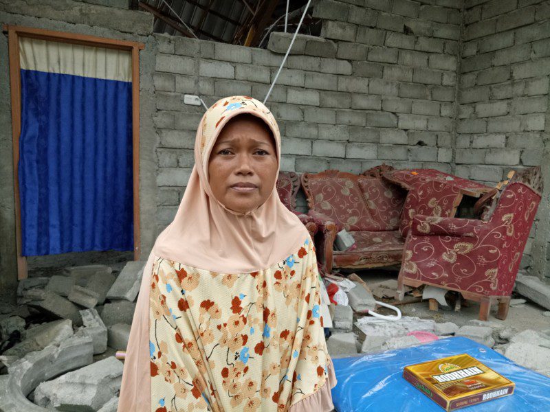 An Indonesia earthquake survivor stands outside her destroyed home in the city of Palu. She has received an emergency shelter kit from Oxfam