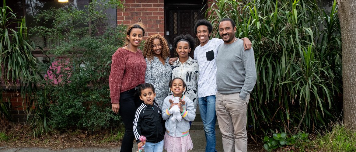 A family stand outside their home smiling.