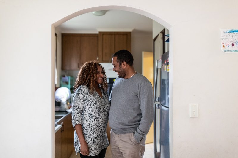 A man and woman stand in a doorway of their home smiling.