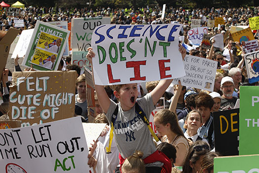 Young boy riding on his friend's shoulders at the #Climatestrike placard with a placard - Science doesn't lie!