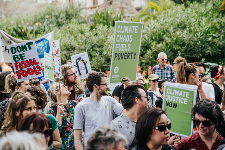 Protesters at the Melbourne #ClimateStrike holding signs that say "Climate Chaos Fules Poverty", "Climate Justice Now" and "Dont be Fossil Fools"