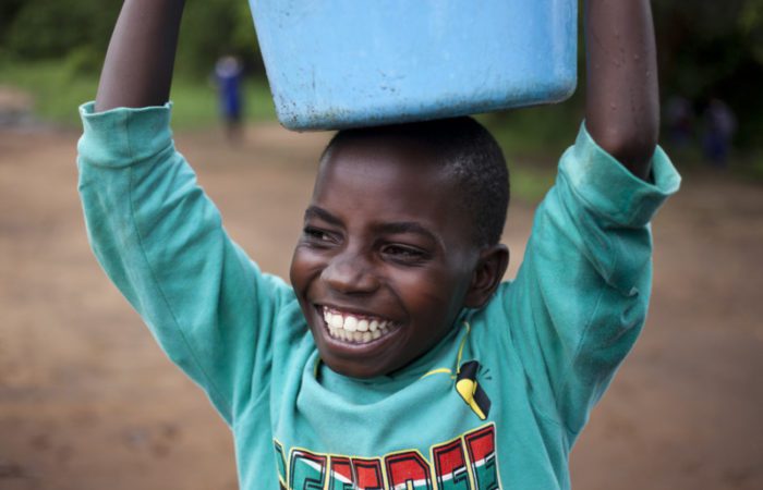 Smiling child holds bucket over his head