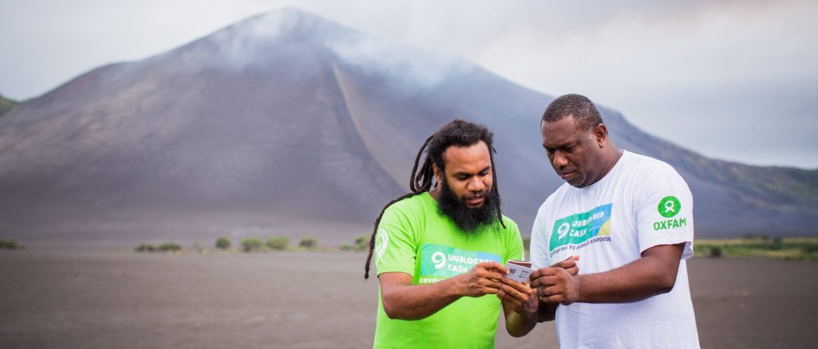 Tanna, Vanuatu: While Vanuatu’s largest volcano, Mount Yasur, smoulders in the distance, Oxfam staff Keith and Sirus test cards and phones that will be distributed to local community members for use within Oxfam’s UnBlocked cash transfer program. Photos: Arlene Bax/Oxfam in Vanuatu Tanna, Vanuatu: While Vanuatu’s largest volcano, Mount Yasur, smoulders in the distance, Oxfam staff Keith and Sirus test cards and phones that will be distributed to local community members for use within Oxfam’s UnBlocked cash transfer program. Photos: Arlene Bax/Oxfam in Vanuatu