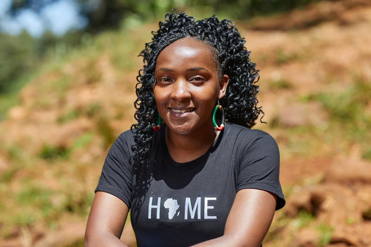 Elizabeth Wanjiru WathutiElizabeth Wanjiru Wathuti founded the Green Generation Initiative in Kenya in 2016 as a way to get more young people interested in climate action and environmental health. Part of her organisation's mission is 'greening' schools in her country by planting trees. To date, the initiative has planted more than 30,000 trees.We met Elizabeth as she visited schools in Nyeri and took part in tree planting, as well as visiting a healthy forest. Elizabeth Wanjiru climate justice activist sits on a hill