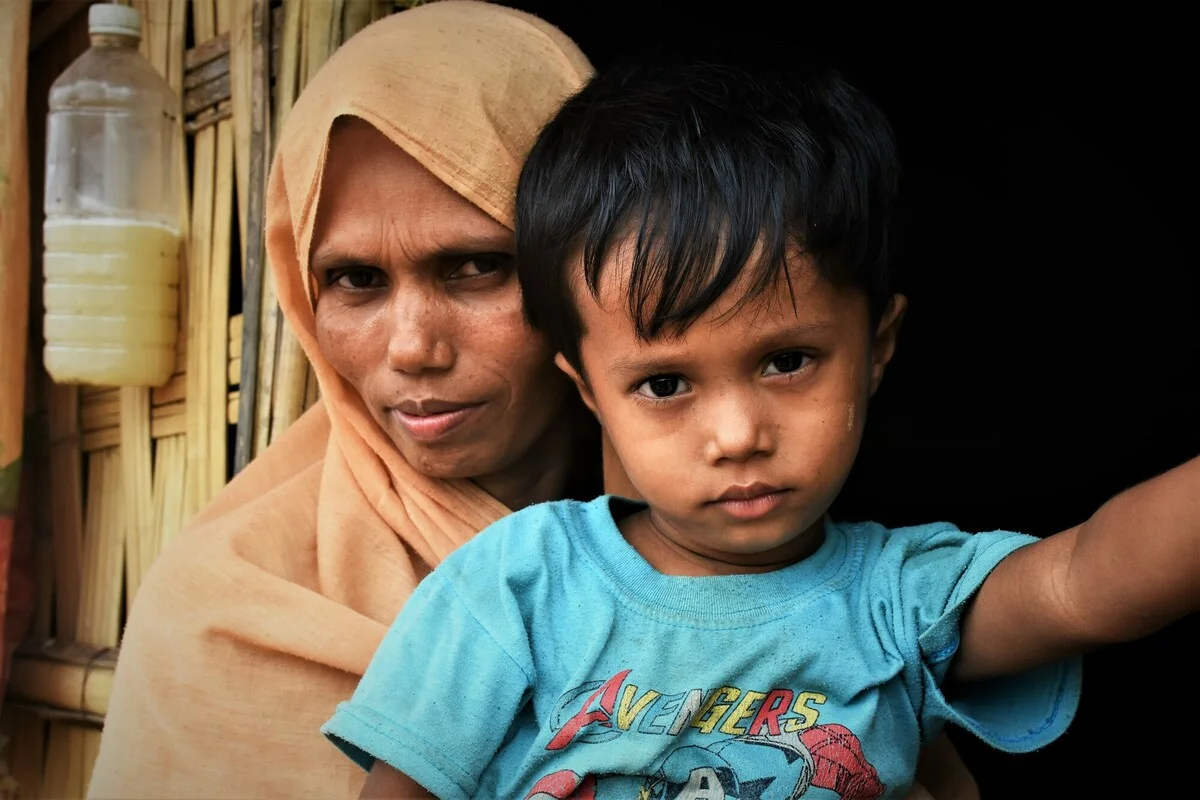 <p>
Single mum Shafika (40) and son Maruf (3) outside their shelter in Cox’s Bazar.</p>
Oxfam is supporting the family with clean water, toilets and solar-powered flood lights.
All names have been changed.
Rohingya single mum Shafika is a refugee living in the camps in CoxÄôs Bazar. She shares a basic shelter made of tarpaulin and bamboo and with her three daughters (aged 20, 14, and 1) and 3-yr-old son. Shafika and her children arrived in Bangladesh around August 2017 Äì they fled Myanmar after her husband was killed. It took them eight days to walk to the border, sleeping in fields out in the open. They arrived empty-handed.
ShafikaÄôs daily routine starts at dawn when she has her first prayer, uses the latrine, washes up and fetches water. She then wakes her children, cooks rice and daal for breakfast Äì occasionally with some dried fish. She doesnÄôt have any spices to cook with and misses the taste of garam masala. She then sits in their home, sometimes gossips with her daughters, prays again and makes lunch. In the afternoon she rests. In the rainy season they spend a lot of time in their home, and the strong winds make it shake, which makes them worry.
Without a man in the family, she feels disadvantaged. The mahjis or local camp leaders disseminate information Äì for example about aid distributions - but those meetings are seen as just for men. She leaves the house rarely Äì to collect aid donations or visit the infirmary Äì as she worries about leaving her daughters alone. She makes the long trip to collect firewood once a month but canÄôt carry such heavy loads as men doing the same chore. She receives a small amount of biofuel monthly to use in their stove but always runs out after a week, so sometimes burns plastic instead.
She and her daughters only have one burqa between them and donÄôt like to go out in public uncovered. This means they can only go out one at a time, or have to borrow another from a neighbour.
Shafika would like more support for women like her. In particular, ways for them to earn money so they can buy essential items and fresh food like green vegetables to supplement their basic rations. She thinks it would be better to have more women in leadership roles making decisions about the community. She also worries about her daughtersÄô future - suitors have approached her but she has no money to provide them with a dowry.