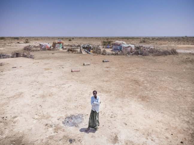 Abdulahi, a young man in a white shirt, stands in the middle of a barren landscape.  