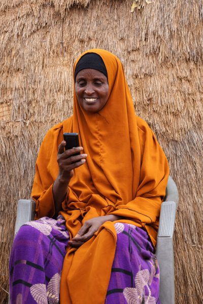 A happy Barey Ibrahim Korone is all smiles as she looks at her mobile phone outside her family hut in Tula Tula, Wajir.