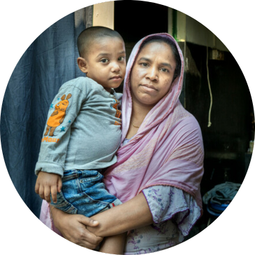 Laily* with her son Safyun (2.5yr). Laily* works as homebased garment worker. She joined garment factory at 12. Since 2019, she started working from home. Laily* brings orders from small factories and do them. Order like bed sheets, pillow covers, and one-piece dresses, these orders are given at home for sewing. With her income she hardly can earn 5000 taka. Mirpur, Dhaka, Bangladesh. Photo: Fabeha Monir/Oxfam Laily* with her son Safyun (2.5yr). Laily* works as homebased garment worker. She joined garment factory at 12. Since 2019, she started working from home. Laily* brings orders from small factories and do them. Order like bed sheets, pillow covers, and one-piece dresses, these orders are given at home for sewing. With her income she hardly can earn 5000 taka. Mirpur, Dhaka, Bangladesh. Photo: Fabeha Monir/Oxfam