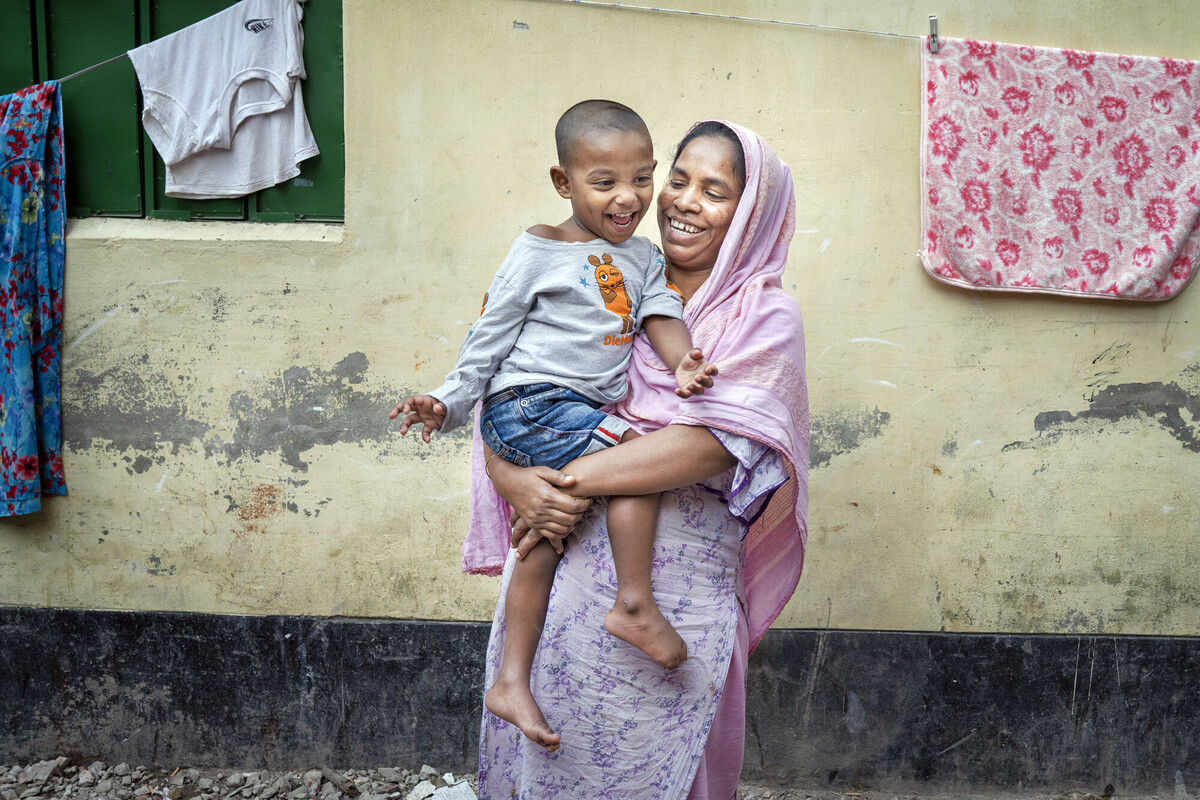 Laily* with her son Safyun (2.5yr). Laily* works as a homebased garment worker. She joined garment factory at 12. Since 2019, she started working from home. Laily* brings orders from small factories and do them. Order like bed sheets, pillow covers, and one-piece dresses, these orders are given at home for sewing. With her income she hardly can earn 5000 taka. Mirpur, Dhaka, Bangladesh. Photo: Fabeha Monir/Oxfam