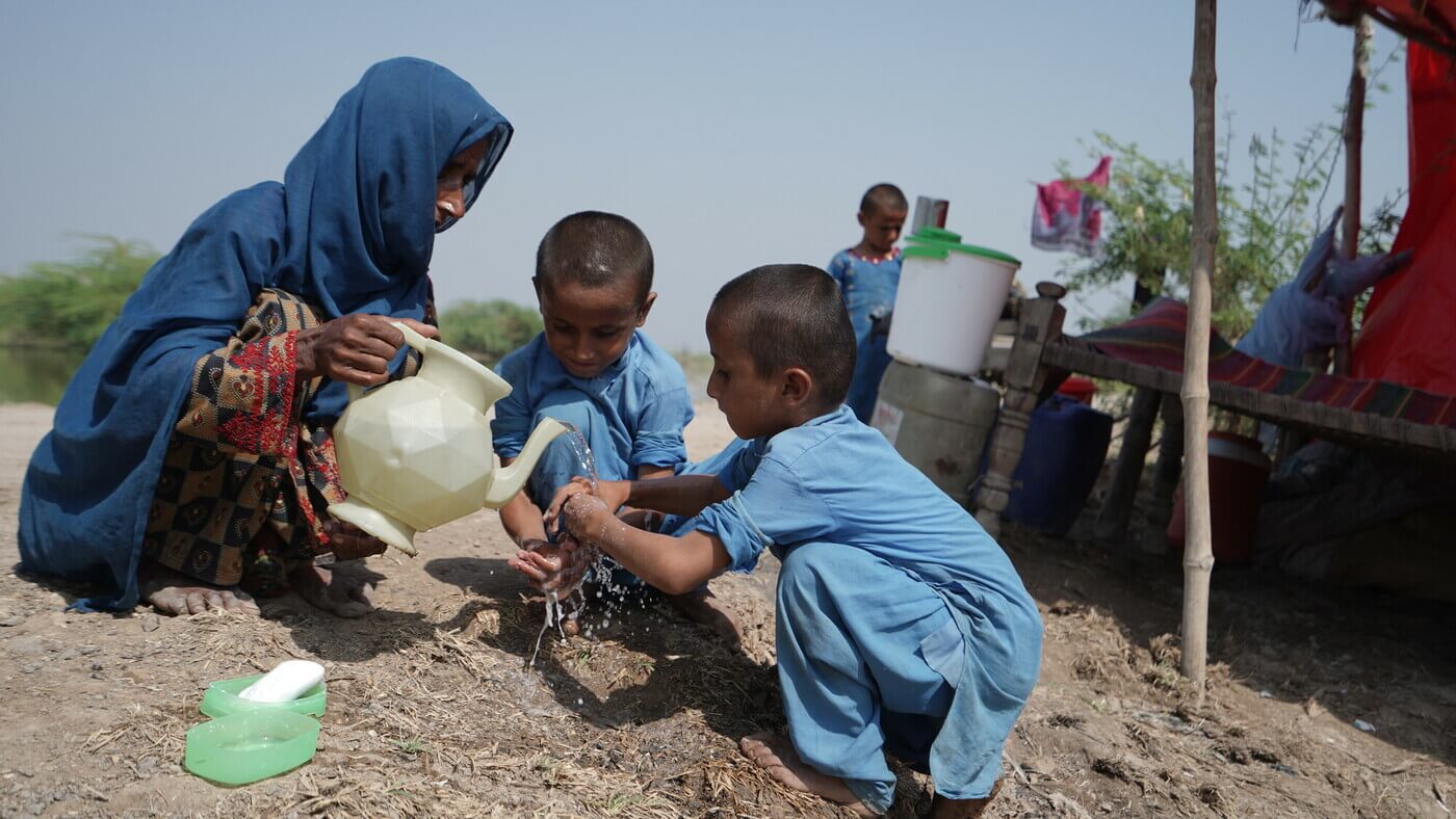 Pakistan: Imam, Wife of Abdul Latif washing her children's hands with floodwater. Photo: Ingenious Captures / Oxfam