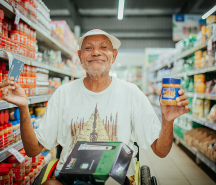 A man stands in a grocery aisle holding a tub of peanut butter and an UnBlocked Cash card.