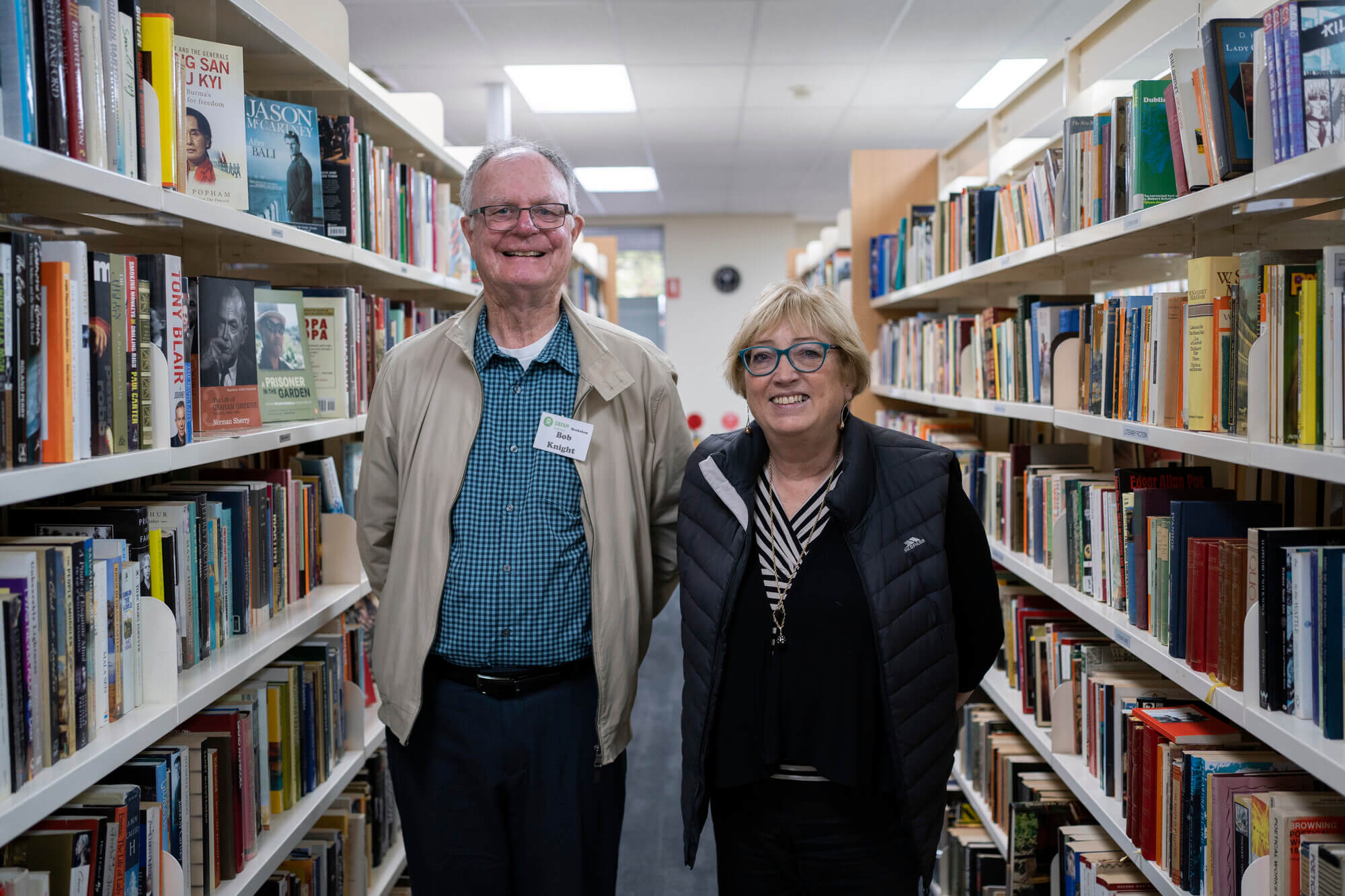 Two volunteers stand in the aisles of a bookshop.