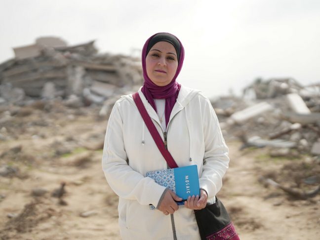 Gaza: Fidaa Shurrab, Director of Projects at Atfaluna for Deaf Society in Rafah stands in front of a destroyed building in Gaza strip while going to work. Photo: Alef Multimedia/Oxfam