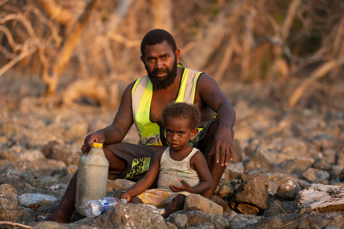 Molpoe, Vanuatu: Antonnie and his son on the beach in Molpoe village, Vanuatu. In 2022, Molpoe was hit by a devastating landslide caused by torrential rain, which has become more frequent due to extreme weather. Photo: Ivan Utahenua/Oxfam
