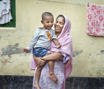Bangladesh: Laily* with her son Safyun (2.5yr). Laily* works as a homebased garment worker. She joined garment factory at 12. Since 2019, she started working from home. Laily* brings orders from small factories and do them. Order like bed sheets, pillow covers, and one-piece dresses, these orders are given at home for sewing. With her income she hardly can earn 5000 taka. Photo: Fabeha Monir/Oxfam Bangladesh: Laily* with her son Safyun (2.5yr). Laily* works as a homebased garment worker. She joined garment factory at 12. Since 2019, she started working from home. Laily* brings orders from small factories and do them. Order like bed sheets, pillow covers, and one-piece dresses, these orders are given at home for sewing. With her income she hardly can earn 5000 taka. Photo: Fabeha Monir/Oxfam