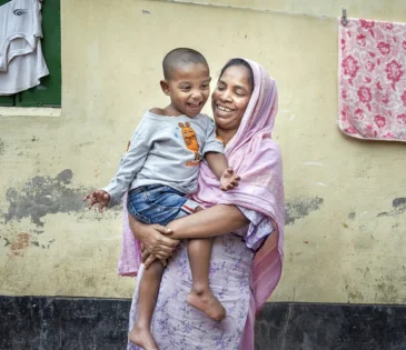 Bangladesh: Laily* with her son Safyun (2.5yr). Laily* works as a homebased garment worker. She joined garment factory at 12. Since 2019, she started working from home. Laily* brings orders from small factories and do them. Order like bed sheets, pillow covers, and one-piece dresses, these orders are given at home for sewing. With her income she hardly can earn 5000 taka. Photo: Fabeha Monir/Oxfam Bangladesh: Laily* with her son Safyun (2.5yr). Laily* works as a homebased garment worker. She joined garment factory at 12. Since 2019, she started working from home. Laily* brings orders from small factories and do them. Order like bed sheets, pillow covers, and one-piece dresses, these orders are given at home for sewing. With her income she hardly can earn 5000 taka. Photo: Fabeha Monir/Oxfam