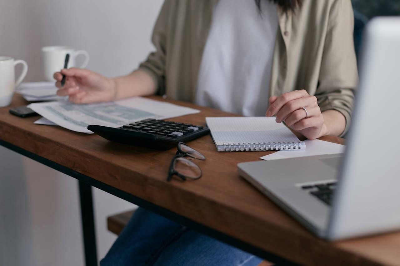 A person sitting in front of a calculator and computer. Photo: Mikhail Nilov/Pexels